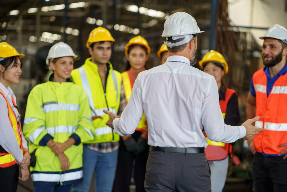 group of diversity engineer factory worker standing in morning meeting with business man manager or executive boss leader team talking and brief in industry manufacturing warehouse