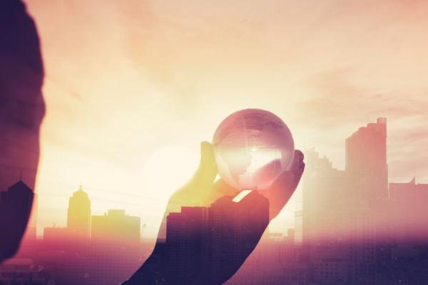 Business man in suit with cityscape montage. Business man in suit with cityscape montage. The man is unrecognizable and you cannot see his face. He is superimposed onto a city skyline at sunset. He is holding a world map globe like a crystal ball.